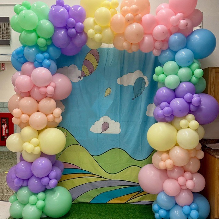 Pastel balloon garland arching over a hand-painted sky backdrop